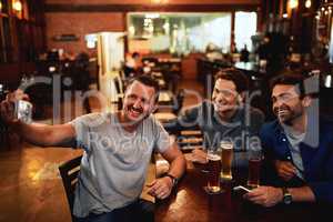 This photo goes out to us. a group of cheerful young friends taking a self portrait together while enjoying beer together at a bar during the night.