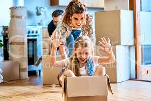 Time to go on an adventure. a cheerful young woman pushing her daughter around in a box imagining its a car inside at home during the day.