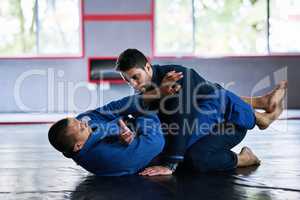 Ground and pound. Full length shot of two young male athletes sparring on the floor of their dojo.