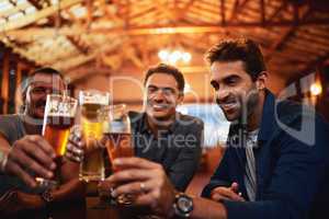 Making memories the best way we know. a group of young friends seated at a table together while enjoying a beer and celebrating with a celebratory toast inside a bar.