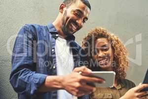Smiling young couple looking, laughing and holding phone together showing a funny social media app. Friends sharing a gossip news article post online. Guy looking at internet web content with girl