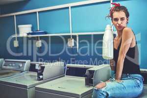 Lets get cleaning. Portrait of an attractive young woman seated on a washing machine while holding bleach to wash her washing with inside of a laundry room during the day.