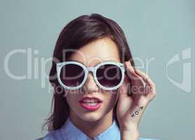 Shes got that x factor. Studio portrait of an attractive young woman posing with with stylish shades against a grey background.
