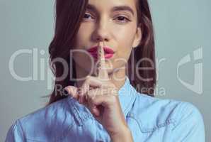 You cant tell a soul. Studio portrait of an attractive young woman posing with her finger on lips against a grey background.