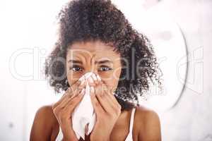 Oh no, could it be flu. an attractive young woman blowing her nose with a tissue at home.