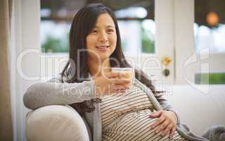 Its strictly decaf for a while. an attractive young pregnant woman drinking an iced coffee while relaxing on the sofa at home.