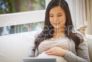 Get all the pregnancy advice you need online. a pregnant woman using a digital tablet at home.