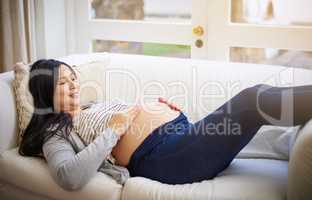 I cant wait to hold you in my arms. an attractive young pregnant woman relaxing on the sofa at home.