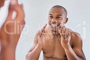 Real men moisturize. a handsome young man applying moisturizer to his face in the bathroom at home.