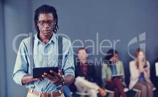 Every move is carefully calculated. a handsome young businessman using a tablet with his colleagues in the background.