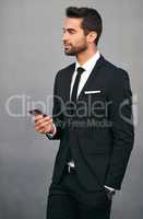 Hes easily reachable. Studio shot of a handsome young businessman using a cellphone against a grey background.