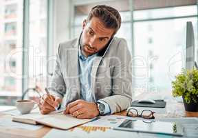 Scheduling all his meetings. a handsome young businessman writing notes while talking on a cellphone in an office.