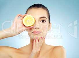 Its beauty benefits are endless. Studio portrait of a beautiful young woman covering her eye with a lemon against a blue background.