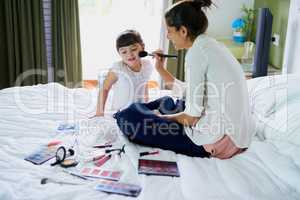 How about some pink rosy cheeks. a mother and her little daughter playing with makeup on the bed at home.