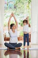 Stretch up high as far as possible. a focused young mother and daughter doing a yoga pose together with their arms raised above their heads.