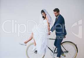 Marriage, one awesome ride. Studio shot of a newly married young couple riding a bicycle together against a gray background.