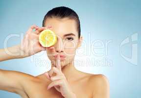 Let me let you in on a little lemony secret. Studio portrait of a beautiful young woman covering her eye with a lemon and putting her finger to her lips.