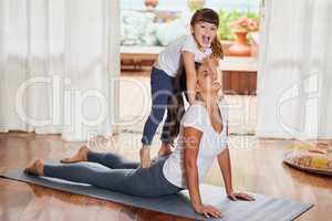 What a interesting pose. a cheerful young woman doing a yoga pose while her young daughter gently stands on her back at home.