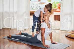 We invented a new pose. a cheerful young woman doing a yoga pose while her young daughter gently stands on her back at home.
