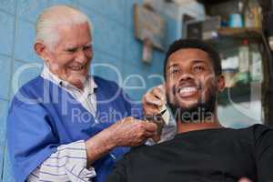 Always a perfectionist when it comes to his customers. a senior man trimming a clients beard in his barber shop.
