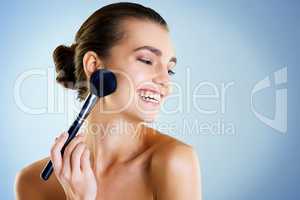 Highlighting her gorgeous features. Studio shot of a beautiful young woman applying makeup with a brush against a blue background.