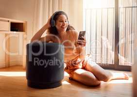 Carefree, relaxed and happy woman relaxing on a video call using her phone and headphones while sitting on the floor. A young excited female listening to an online podcast or browsing social media