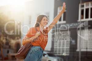 Waving for a taxi, waiting in the street for a ride outside. Smiling urban woman wants to travel downtown for work or fun with a cab. Lady gestures for transportation with confident arm raised.