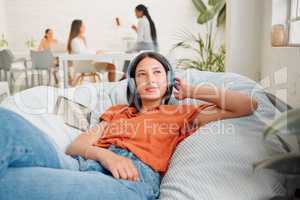 Creative wearing headphones, listening to music and relaxing with zen songs or podcast to help with thinking, planning and inspiration. Motivated, inspired and ambitous woman lying on office bean bag