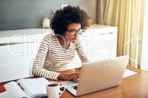 Shes in work mode. a confident young woman working on her laptop while drinking a cup of coffee at home during the day.