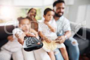 Closeup of remote control with family watching tv in their living room together. Parents and kids relaxing on the sofa enjoying a movie, series or cartoons in the lounge at home while bonding