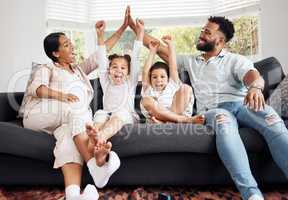 Happy parents and excited children celebrate on the sofa while watching tv. Fun family time, relaxing at home and bonding. Mother and father high five, kids cheer for sports team win.