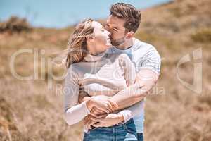 Hugging, embracing and in love young couple spending a romantic summer day in nature together. Happy partners on a getaway kissing, smiling and relaxing outdoors enjoying and loving the sunshine