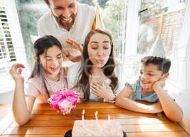 Birthday, family and celebration with a woman blowing the candles on her cake. Husband and kids spoiling mom and making her feel happy on her special day mothers day while having a party at home