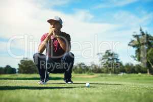 On the fairway. a focused young male golfer looking at a golf ball while being seated on the grass outside during the day.