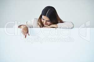 If you could direct your attention over here... Studio shot of an attractive young businesswoman pointing at copy space on a blank placard.