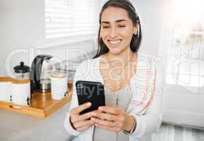 Woman browsing, texting and reading on a phone in her kitchen at home. Smiling woman on social media online app, networking and messaging contacts while smiling at a funny post, meme or videos
