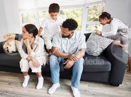 Frustrated, annoyed and irritated couple sitting on the couch with their hyperactive, noisy and naughty kids fooling around on the sofa at home. Man and woman feeling tired while their children play