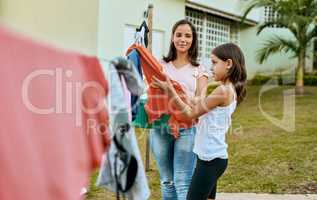 It goes quicker when they do it together. a mother and daughter hanging up laundry together outside.
