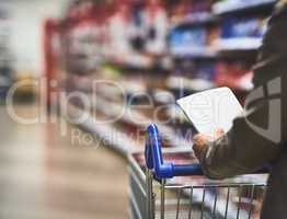Use a list and avoid over spending. a woman shopping with a list in a grocery store.