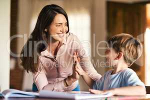 Encouragement is vital in the learning process. a mother giving her son a high five while helping him with his homework.