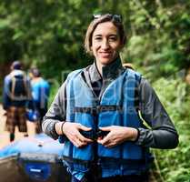 She is ready to go rafting. Portrait of a cheerful young woman putting on a life jacket to go river rafting outside during the day.