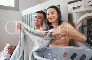 Folding laundry, day chores and house work of a happy, smiling and positive couple cleaning. Sitting, cheerful and loving partners washing clothes and working together on a relaxed day at home inside