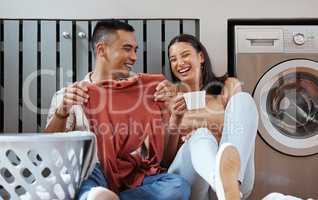 Carefree and funny couple doing laundry and relaxing together at home in the morning. Silly, goofy and playful lovers laughing and giggling while cleaning the washing, and doing house chores