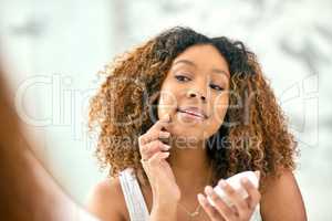 Now for the finishing touches. a confident young woman applying skin cream on her face while looking into the mirror in the bathroom at home.