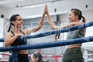 High five with female boxing athlete or fighter and gym partner in the ring of a health and sports club. Young women motivating and congratulating one another after training, sparring and exercising