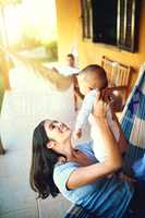 Flying around like an airplane. a cheerful young mother holding her baby infant son while smiling at him outside at home.