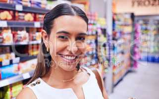 Shopping, groceries and consumerism with a young woman in a grocery store, retail shop or supermarket aisle. Closeup portrait of a female standing with packed shelves of consumables in the background