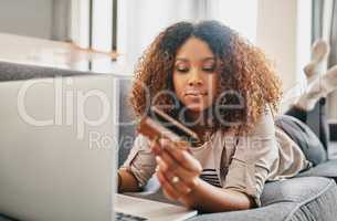 Shopping has never been easier. a focused young woman doing online shopping on her laptop while lying on a couch at home during the day.