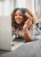 Time to treat myself. a cheerful young woman doing online shopping on her laptop while lying on a couch at home during the day.