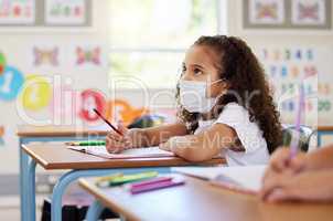 Education, classroom and learning with covid face mask on girl doing school work, writing and reading at her desk in elementary class. Elementary child wearing protection to stop the spread of virus